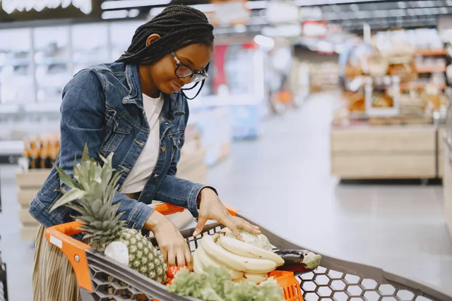 A woman shops for fresh fruits and vegetables in a supermarket, pushing a cart filled with groceries. Interpreting published retail shopper research